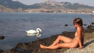 A naked girl is having fun on the riverbank, sunbathing
