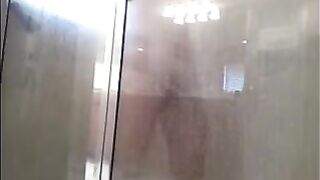 A man washes himself in the shower, unaware of being watched